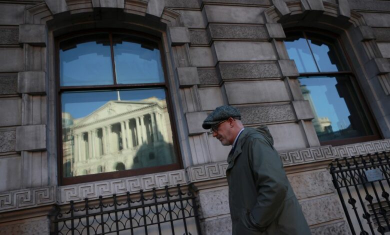 A man walks past a window reflecting the Bank of England, in London