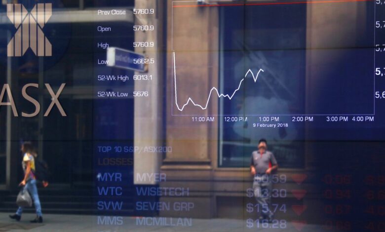 FILE PHOTO - Pedestrians are reflected in a window in front of a board displaying stock prices at the Australian Securities Exchange in Sydney