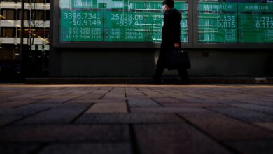 A man wearing a protective mask, amid the coronavirus disease (COVID-19) outbreak, walks past an electronic board displaying Shanghai Composite index, Nikkei index and Dow Jones Industrial Average outside a brokerage in Tokyo