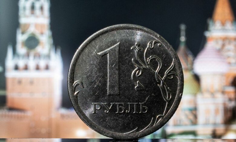 A Russian one rouble coin is pictured in front of a monitor showing the Kremlin