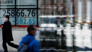 Passersby wearing protective face masks walk past a stock quotation board, in Tokyo