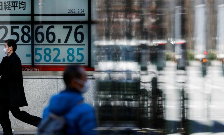 Passersby wearing protective face masks walk past a stock quotation board, in Tokyo