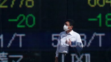 A man wearing a protective mask is reflected on an electronic board displaying stock prices outside a brokerage in Tokyo