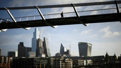 The City of London financial district is seen as a person walks over Millennium Bridge in London