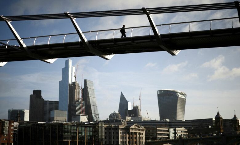 The City of London financial district is seen as a person walks over Millennium Bridge in London