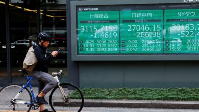 A man on a bicycle stands in front of an electronic board showing Shanghai stock index, Nikkei share price index and  Dow Jones Industrial Average outside a brokerage in Tokyo