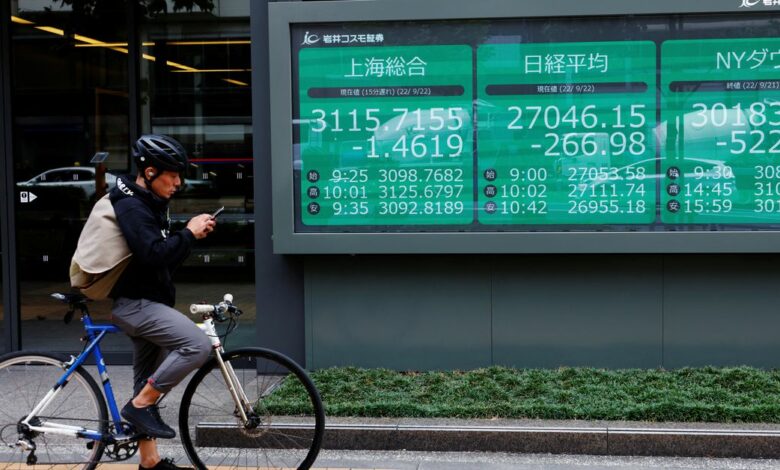 A man on a bicycle stands in front of an electronic board showing Shanghai stock index, Nikkei share price index and  Dow Jones Industrial Average outside a brokerage in Tokyo