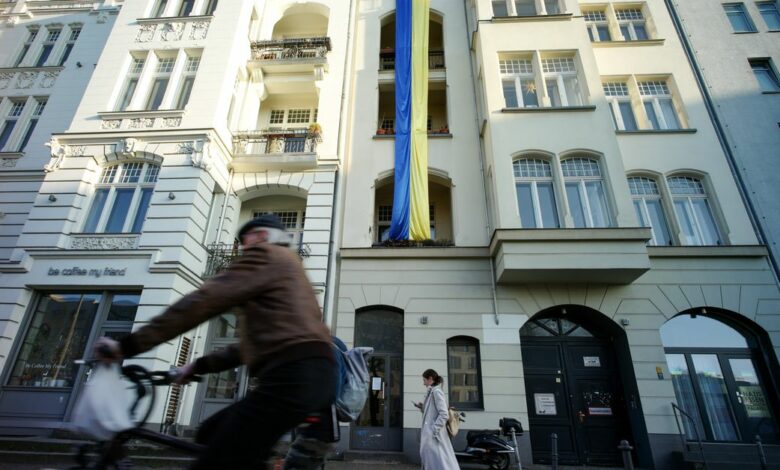Pedestrians walk past a Ukrainian flag hanging in support of the country on an apartment building in Berlin