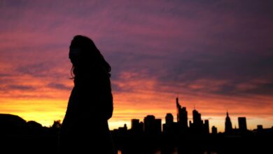 A woman wearing a protective mask walks past the skyline of the financial district during sunset as the spread of the coronavirus disease (COVID-19) continues in Frankfurt