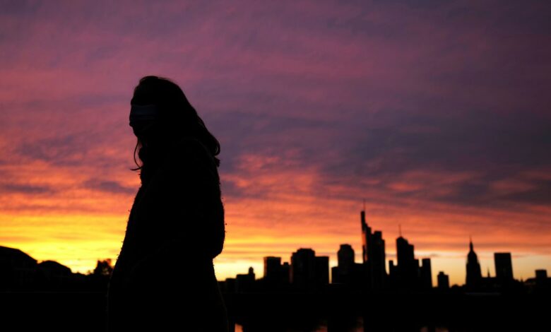 A woman wearing a protective mask walks past the skyline of the financial district during sunset as the spread of the coronavirus disease (COVID-19) continues in Frankfurt