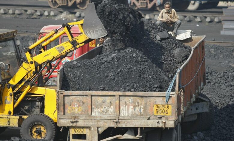 A worker sits on a truck being loaded with coal at a railway coal yard on the outskirts of Ahmedabad